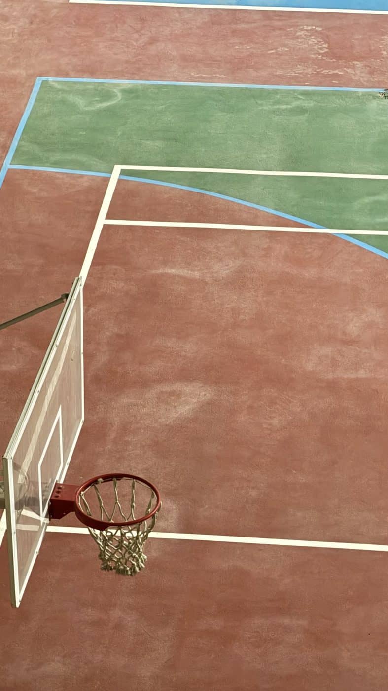 An empty basketball court seen from above, red court and green backboard