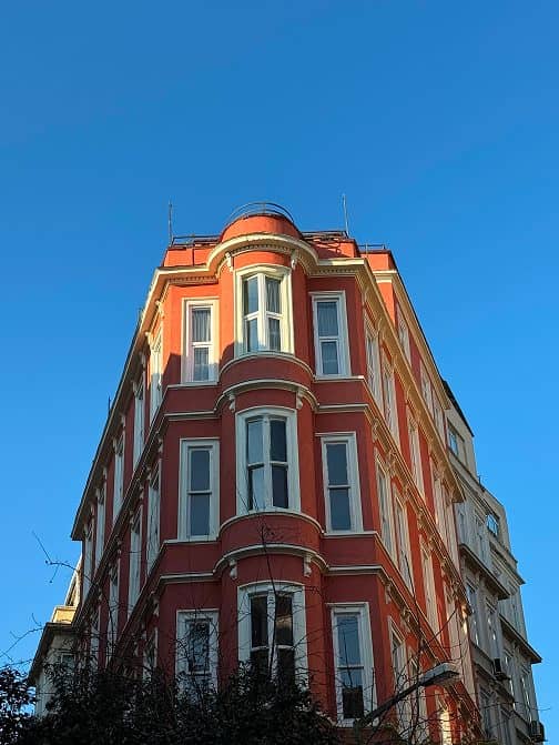A red corner building with white bay windows against a clear blue sky