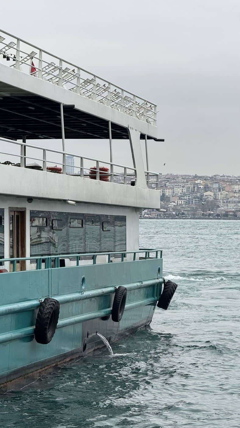 A ferry on open water with a city skyline behind it